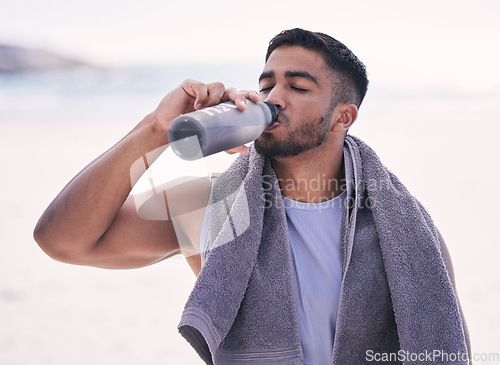 Image of Fitness, sports and man drinking water at the beach after running, training or morning cardio workout with bottle. Exercise, break and thirsty Indian male runner or person with hydration drink at sea