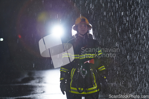 Image of A determined female firefighter in a professional uniform striding through the dangerous, rainy night on a daring rescue mission, showcasing her unwavering bravery and commitment to saving lives.