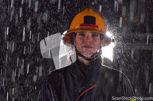 Image of A determined female firefighter in a professional uniform striding through the dangerous, rainy night on a daring rescue mission, showcasing her unwavering bravery and commitment to saving lives.