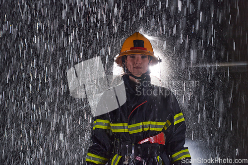 Image of A determined female firefighter in a professional uniform striding through the dangerous, rainy night on a daring rescue mission, showcasing her unwavering bravery and commitment to saving lives.