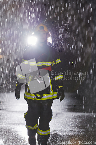 Image of A determined female firefighter in a professional uniform striding through the dangerous, rainy night on a daring rescue mission, showcasing her unwavering bravery and commitment to saving lives.