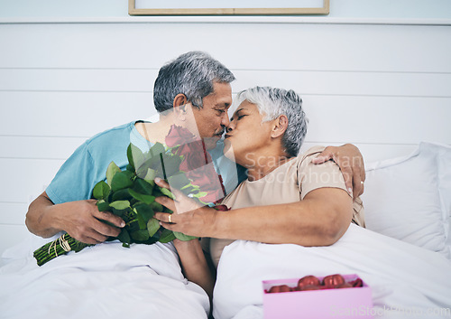 Image of Love, elderly couple and kiss with roses in bed, romance and affection in home. Flowers, senior man and woman in bedroom for intimacy, care and enjoying quality time together with floral bouquet gift