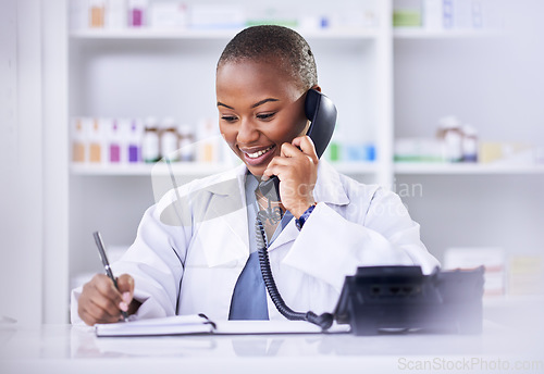 Image of Black woman, phone call and pharmacist writing in notebook for Telehealth consultation at the pharmacy. Happy African female person, medical or healthcare professional talking on telephone at clinic