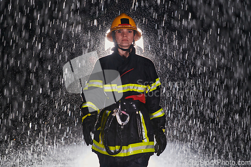 Image of A determined female firefighter in a professional uniform striding through the dangerous, rainy night on a daring rescue mission, showcasing her unwavering bravery and commitment to saving lives.