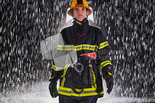 Image of A determined female firefighter in a professional uniform striding through the dangerous, rainy night on a daring rescue mission, showcasing her unwavering bravery and commitment to saving lives.