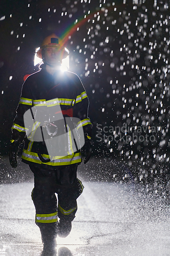 Image of A determined female firefighter in a professional uniform striding through the dangerous, rainy night on a daring rescue mission, showcasing her unwavering bravery and commitment to saving lives.