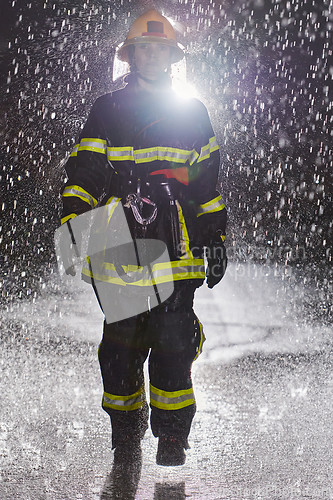 Image of A determined female firefighter in a professional uniform striding through the dangerous, rainy night on a daring rescue mission, showcasing her unwavering bravery and commitment to saving lives.