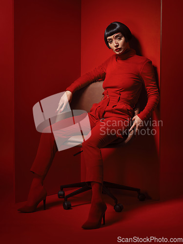 Image of Chair, fashion and a model woman on red background in studio for elegant, chic or trendy style. Aesthetic, art and confident beauty with an edgy or classy young person in a unique clothes or suit