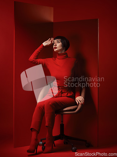 Image of Thinking, fashion and a model woman on red background in studio for elegant, chic or trendy style. Aesthetic, art and beauty with an edgy person in unique clothes suit, makeup and cosmetics on chair