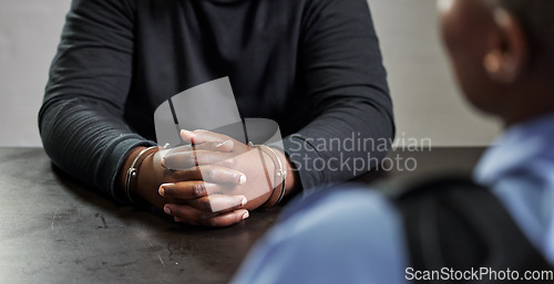 Image of Criminal, hands and handcuffs and table for interrogation, questions or accusation with officer in room. Police talking to prisoner, gangster or thief for security, discussion or arrest in prison