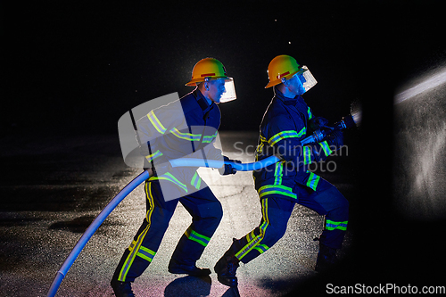 Image of Firefighters using a water hose to eliminate a fire hazard. Team of female and male firemen in dangerous rescue mission.