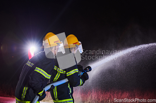 Image of Firefighters using a water hose to eliminate a fire hazard. Team of female and male firemen in dangerous rescue mission.