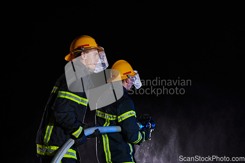 Image of Firefighters using a water hose to eliminate a fire hazard. Team of female and male firemen in dangerous rescue mission.