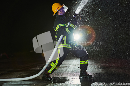 Image of Firefighter using a water hose to eliminate a fire hazard. Team of firemen in the dangerous rescue mission.