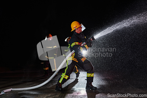 Image of Firefighters using a water hose to eliminate a fire hazard. Team of female and male firemen in dangerous rescue mission.