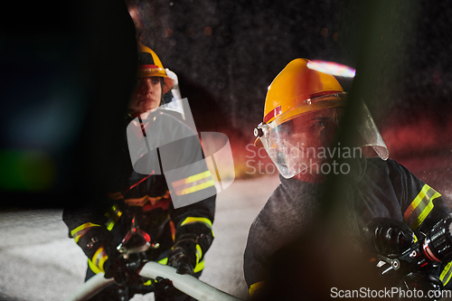 Image of Firefighters using a water hose to eliminate a fire hazard. Team of female and male firemen in dangerous rescue mission.