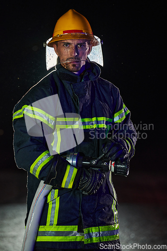 Image of Firefighter using a water hose to eliminate a fire hazard. Team of female and male firemen in dangerous rescue mission.