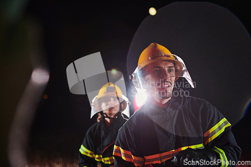 Image of Firefighters using a water hose to eliminate a fire hazard. Team of female and male firemen in dangerous rescue mission.