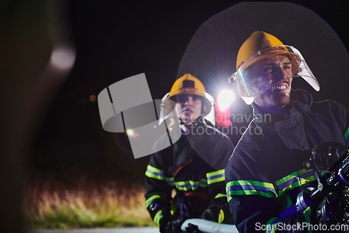 Image of Firefighters using a water hose to eliminate a fire hazard. Team of female and male firemen in dangerous rescue mission.