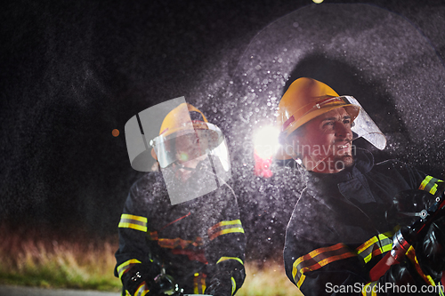 Image of Firefighters using a water hose to eliminate a fire hazard. Team of female and male firemen in dangerous rescue mission.