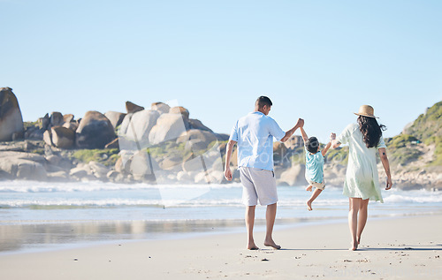 Image of Family, parents and lifting a child at the beach for fun, adventure and play on holiday. Behind a woman, man and young kid walking on sand or swinging on vacation at the ocean, nature or outdoor