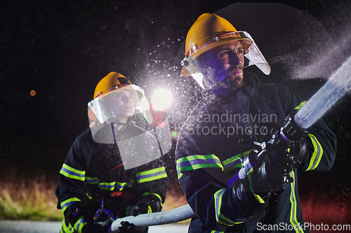 Image of Firefighters using a water hose to eliminate a fire hazard. Team of female and male firemen in dangerous rescue mission.