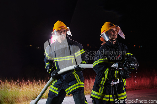 Image of Firefighters using a water hose to eliminate a fire hazard. Team of female and male firemen in dangerous rescue mission.