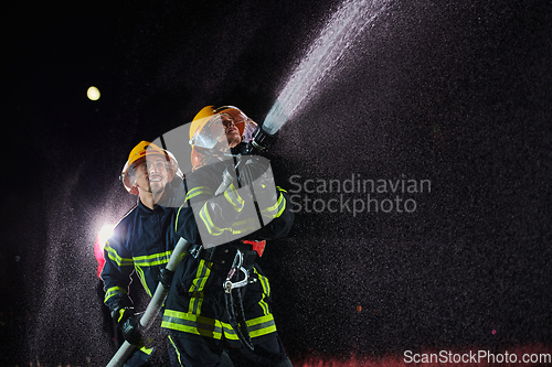 Image of Firefighters using a water hose to eliminate a fire hazard. Team of female and male firemen in dangerous rescue mission.