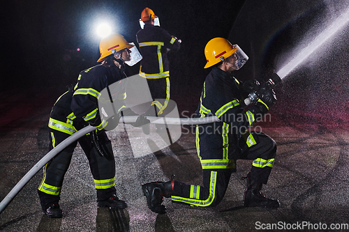 Image of Firefighters using a water hose to eliminate a fire hazard. Team of female and male firemen in dangerous rescue mission.