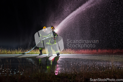 Image of Firefighters using a water hose to eliminate a fire hazard. Team of female and male firemen in dangerous rescue mission.