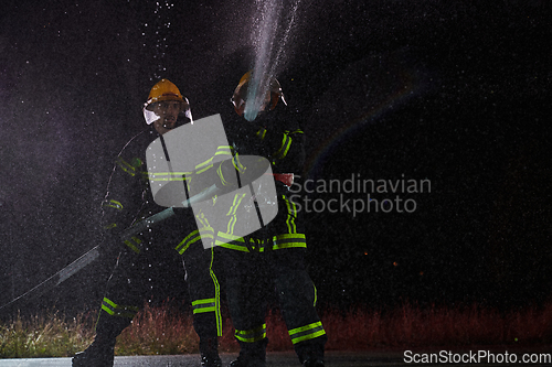 Image of Firefighters using a water hose to eliminate a fire hazard. Team of female and male firemen in dangerous rescue mission.