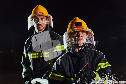 Image of Firefighters using a water hose to eliminate a fire hazard. Team of female and male firemen in dangerous rescue mission.