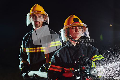 Image of Firefighters using a water hose to eliminate a fire hazard. Team of female and male firemen in dangerous rescue mission.