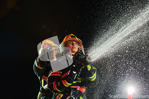 Image of Firefighters using a water hose to eliminate a fire hazard. Team of female and male firemen in dangerous rescue mission.