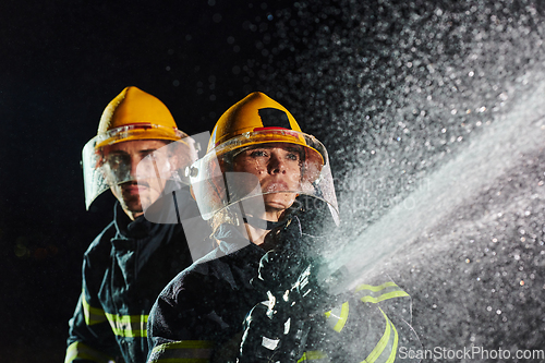 Image of Firefighters using a water hose to eliminate a fire hazard. Team of female and male firemen in dangerous rescue mission.