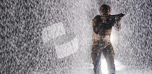 Image of Army soldier in Combat Uniforms with an assault rifle, plate carrier and combat helmet going on a dangerous mission on a rainy night.