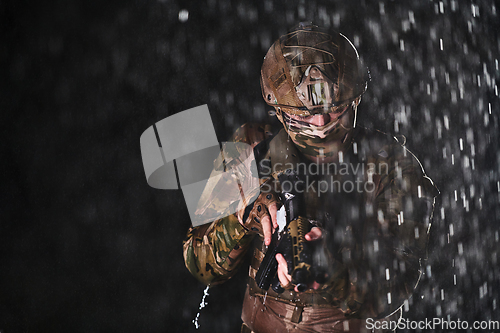 Image of Army soldier in Combat Uniforms with an assault rifle, plate carrier and combat helmet going on a dangerous mission on a rainy night.