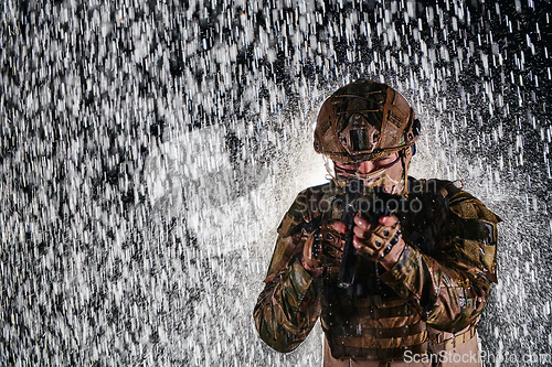 Image of Army soldier in Combat Uniforms with an assault rifle, plate carrier and combat helmet going on a dangerous mission on a rainy night.