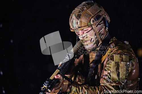 Image of Army soldier in Combat Uniforms with an assault rifle, plate carrier and combat helmet going on a dangerous mission on a rainy night.