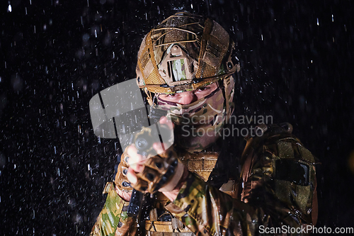 Image of Army soldier in Combat Uniforms with an assault rifle, plate carrier and combat helmet going on a dangerous mission on a rainy night.