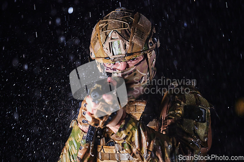 Image of Army soldier in Combat Uniforms with an assault rifle, plate carrier and combat helmet going on a dangerous mission on a rainy night.