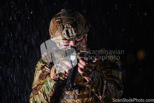 Image of Army soldier in Combat Uniforms with an assault rifle, plate carrier and combat helmet going on a dangerous mission on a rainy night.