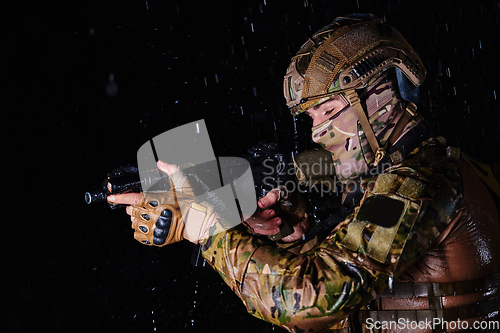 Image of Army soldier in Combat Uniforms with an assault rifle, plate carrier and combat helmet going on a dangerous mission on a rainy night.