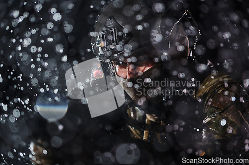 Image of Army soldier in Combat Uniforms with an assault rifle, plate carrier and combat helmet going on a dangerous mission on a rainy night.