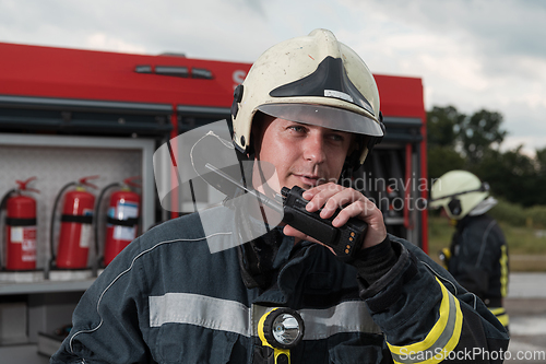 Image of Fireman using walkie talkie at rescue action fire truck and fireman's team in background