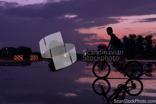 Image of Lonely children silhouette on bike, boy riding bicycle on reflective water. Background beautiful sunset.