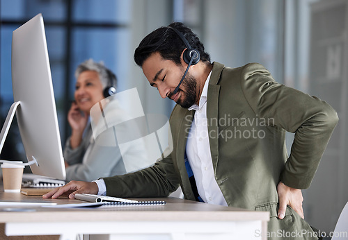 Image of Back pain, call center and tired man with stress, burnout and fatigue at crm or contact us help desk. Asian agent or consultant person in telemarketing, sales and customer service with pain or injury
