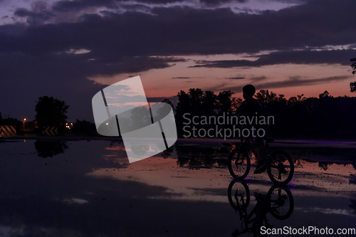 Image of Lonely children silhouette on bike, boy riding bicycle on reflective water. Background beautiful sunset.