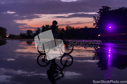 Image of Lonely children silhouette on bike, boy riding bicycle on reflective water. Background beautiful sunset.