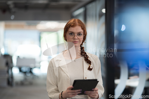 Image of A young business woman with orange hair self-confident, fully engaged in working on a tablet, exuding creativity, ambition and a lively sense of individuality